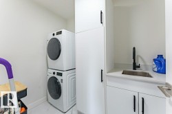 Laundry area featuring a stacked washer and dryer, white cabinetry with black hardware, a stainless steel sink with a matte black faucet, and a light-colored countertop - 
