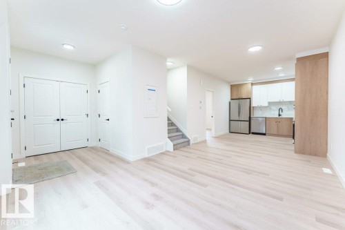 Open-concept living space featuring light wood-finish flooring, recessed ceiling lighting, a two-tone kitchen with stainless steel appliances, and a built-in staircase - 6920/6922 106 Street, Edmonton, AB - Indoor
