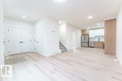Open-concept living space featuring light wood-finish flooring, recessed ceiling lighting, a two-tone kitchen with stainless steel appliances, and a built-in staircase - 