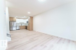 Open-concept living space featuring wood-finish flooring, a modern kitchen with stainless steel appliances, two-tone cabinetry, and a full backsplash - 