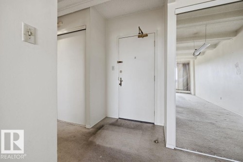 Foyer entrance featuring a solid white door with a brass door closer and multiple locks, alongside a mirrored wall revealing a spacious room with concrete ceilings - 1208 9918 101 Street, Edmonton, AB - Indoor Photo Showing Other Room