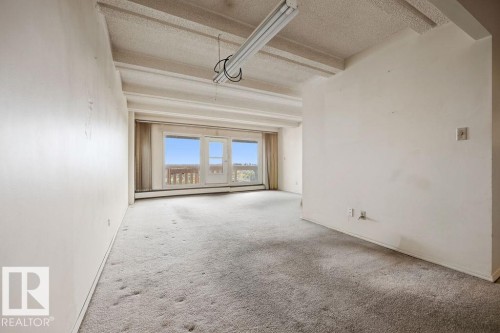 Bright interior space featuring a full-width balcony access with a scenic backdrop, light-toned carpeting, and an exposed beam ceiling - 1208 9918 101 Street, Edmonton, AB - Indoor Photo Showing Other Room