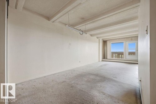 Room featuring light-colored wall-to-wall carpeting, exposed ceiling beams, and a full-light exterior door with an upper window - 1208 9918 101 Street, Edmonton, AB - Indoor
