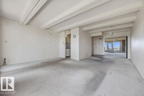 Spacious living area featuring exposed ceiling beams, wall-to-wall carpeting, and a mirrored wall - 1208 9918 101 Street, Edmonton, AB - Indoor Photo Showing Other Room