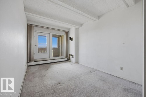Room featuring a sliding glass door with an integrated door, light-colored carpeting, white painted walls, and a textured ceiling with exposed beams - 1208 9918 101 Street, Edmonton, AB -  Photo Showing Other Room