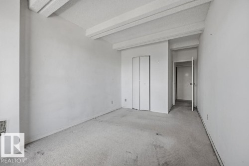 Room featuring a textured ceiling with exposed beams, light-colored carpet flooring, white walls, bi-fold closet doors, and an entryway - 1208 9918 101 Street, Edmonton, AB - Indoor Photo Showing Other Room