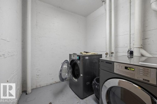 Dedicated laundry area featuring a front-loading washer and dryer, painted concrete walls, and visible utility piping - 1208 9918 101 Street, Edmonton, AB - Indoor Photo Showing Laundry Room