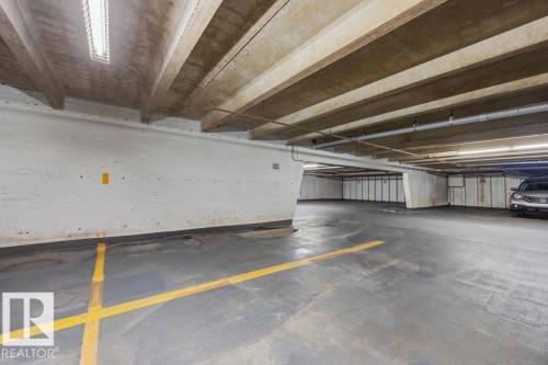 Concrete parking garage featuring exposed beam ceiling, fluorescent lighting, painted concrete walls, and marked parking spaces - 1208 9918 101 Street, Edmonton, AB - Indoor