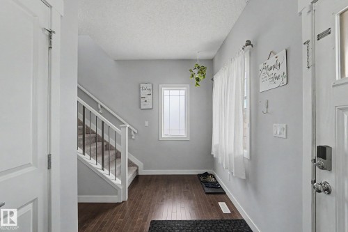 Entryway featuring wood-finish flooring, light grey walls, and a staircase with white risers and dark metal spindles - 18144 76 Street, Edmonton, AB - Indoor Photo Showing Other Room