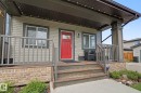 Covered porch entrance with a vibrant red door, horizontal siding, full-light windows, composite deck stairs, and a stone-clad foundation - 18144 76 Street, Edmonton, AB  - Outdoor With Deck Patio Veranda 