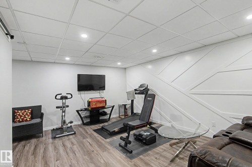Spacious recreation room featuring wood-finish flooring, recessed lighting, and a decorative accent wall with geometric paneling - 18144 76 Street, Edmonton, AB - Indoor Photo Showing Gym Room