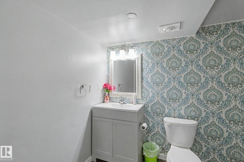 Bathroom featuring a patterned accent wall, white toilet, and a vanity with a rectangular sink - 18144 76 Street, Edmonton, AB - Indoor Photo Showing Bathroom