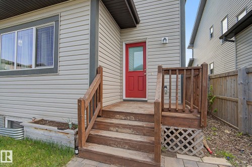 Red entry door with an exterior light fixture, wood deck, and wood railing - 18144 76 Street, Edmonton, AB - Outdoor With Exterior