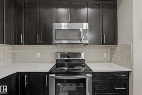 Kitchen featuring dark wood-finish cabinetry, light-toned countertops, and a subway tile backsplash - 18144 76 Street, Edmonton, AB - Indoor Photo Showing Kitchen