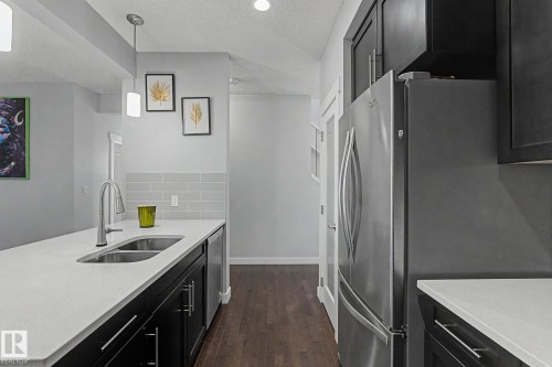Modern kitchen featuring dark wood cabinetry, stainless steel appliances, white countertops, and wood-finish flooring - 18144 76 Street, Edmonton, AB - Indoor Photo Showing Kitchen With Double Sink