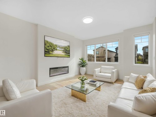 Spacious living area featuring light wood-finish flooring, an integrated linear electric fireplace, and large windows - 1518 Siskin Link Link, Edmonton, AB - Indoor Photo Showing Living Room