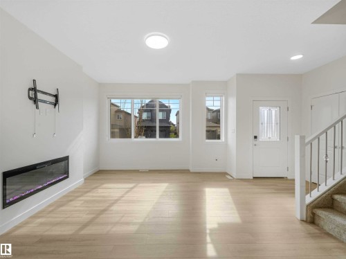 Bright living area featuring wood-finish flooring, an electric fireplace, white trim, and a staircase with a metal railing - 1518 Siskin Link Link, Edmonton, AB - Indoor With Fireplace