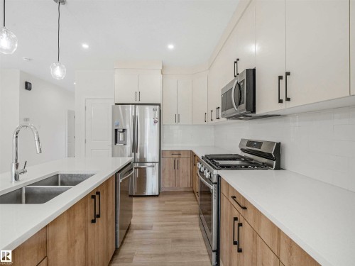 Contemporary kitchen featuring a dual-tone cabinetry design, stainless steel appliances, a double basin sink with a chrome faucet, light countertops, and recessed lighting - 1518 Siskin Link Link, Edmonton, AB - Indoor Photo Showing Kitchen With Double Sink With Upgraded Kitchen