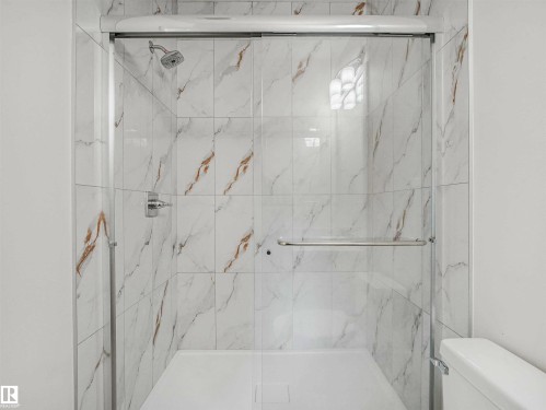 Glass-enclosed shower featuring white and gold veined tile, a white shower pan, a rainfall showerhead, and a chrome grab bar - 1518 Siskin Link Link, Edmonton, AB - Indoor Photo Showing Bathroom