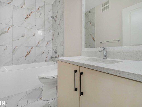 Bathroom featuring a light-toned vanity with integrated sink, chrome faucet, and expansive wall mirror - 1518 Siskin Link Link, Edmonton, AB - Indoor Photo Showing Bathroom