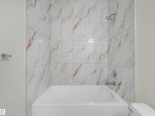 Bathtub and shower combination featuring floor-to-ceiling white and gold veined tile - 1518 Siskin Link Link, Edmonton, AB - Indoor Photo Showing Bathroom
