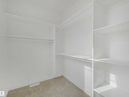 Walk-in closet featuring white walls, light-toned carpet flooring, built-in shelving, and clothes hanging rods - 1518 Siskin Link Link, Edmonton, AB - Indoor With Storage