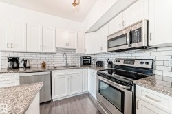 Kitchen featuring white shaker-style cabinetry, granite countertops, subway tile backsplash, stainless steel appliances, and wood-finish flooring - 