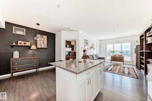 White kitchen island with a granite-style countertop, dark wood-finish flooring, and recessed lighting - 316 10518 113 Street, Edmonton, AB - Indoor