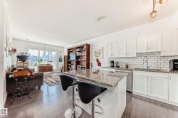 Open-concept living area featuring a kitchen island with seating, white shaker cabinetry, subway tile backsplash, and a large window overlooking city architecture - 