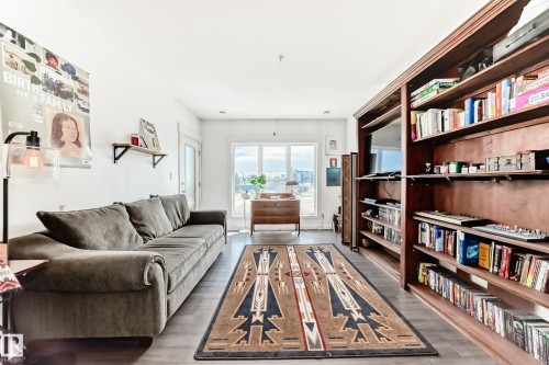 Living area featuring wide plank wood-finish flooring, a full-height built-in shelving unit, and a window with urban scenery - 316 10518 113 Street, Edmonton, AB - Indoor