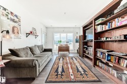 Living area featuring wide plank wood-finish flooring, a full-height built-in shelving unit, and a window with urban scenery - 
