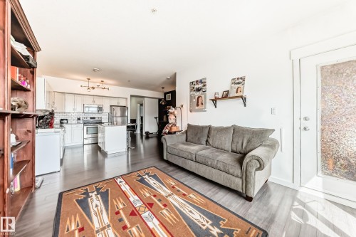 Open-concept living space featuring wood-finish flooring, a contemporary kitchen with white cabinetry, stainless steel appliances, and a central island - 316 10518 113 Street, Edmonton, AB - Indoor Photo Showing Living Room