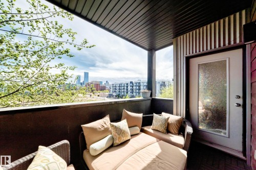 Covered outdoor balcony featuring a dark wood-finish ceiling, urban cityscape scenery, and a frosted glass door - 316 10518 113 Street, Edmonton, AB -  With Exterior