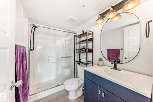 Bathroom featuring a white shower stall with glass enclosure, a toilet, and a vanity with a white countertop and navy blue cabinetry - 316 10518 113 Street, Edmonton, AB - Indoor Photo Showing Bathroom