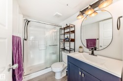 Bathroom featuring a white shower stall with glass enclosure, a toilet, and a vanity with a white countertop and navy blue cabinetry - 