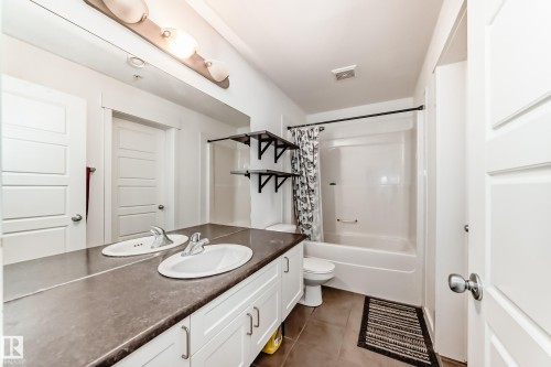 Bathroom featuring a dual-sink vanity with white cabinetry and a dark countertop, a white acrylic tub and shower combination, and brown tile flooring - 316 10518 113 Street, Edmonton, AB - Indoor Photo Showing Bathroom