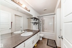 Bathroom featuring a dual-sink vanity with white cabinetry and a dark countertop, a white acrylic tub and shower combination, and brown tile flooring - 