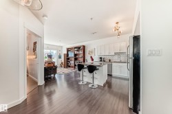 Open-concept living area featuring dark wood-finish flooring, white kitchen cabinetry, subway tile backsplash, a kitchen island with seating, and a contemporary light fixture - 