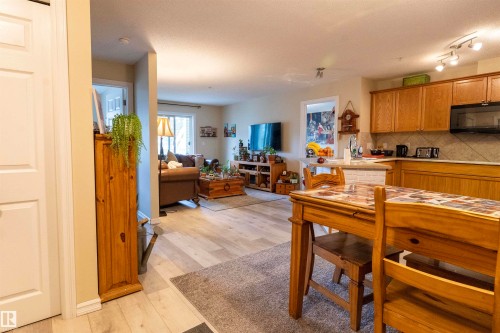 Spacious open-concept living area featuring light wood-finish flooring, a kitchen with wood cabinetry and tile backsplash, and recessed lighting - 203 4403 23 Street, Edmonton, AB - Indoor