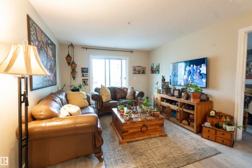 Living area featuring light wood-finish flooring, light neutral wall paint, and a sliding glass door - 203 4403 23 Street, Edmonton, AB - Indoor Photo Showing Living Room