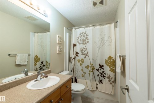 Bathroom featuring a single vanity with a light-toned countertop, wood-finish cabinetry, and an integrated sink - 203 4403 23 Street, Edmonton, AB - Indoor Photo Showing Bathroom
