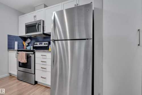Kitchen featuring white cabinetry, stainless steel appliances, blue subway tile backsplash, light-toned countertops, and wood-finish flooring - 128 390 Windermere Road, Edmonton, AB - Indoor Photo Showing Kitchen