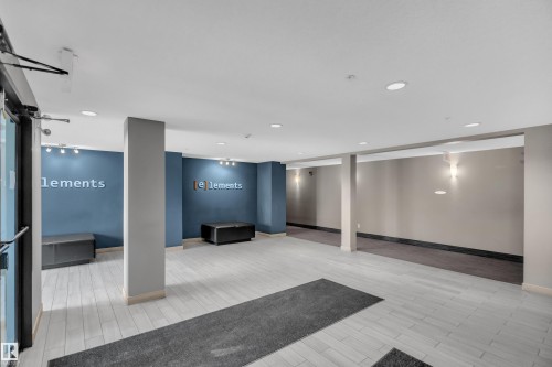 Spacious communal entry foyer featuring light-toned tile flooring, recessed ceiling lighting, and blue accent walls with integrated track lighting - 128 390 Windermere Road, Edmonton, AB - Indoor Photo Showing Other Room