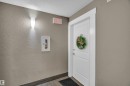 Entry corridor featuring a white panel door with modern hardware, textured wall finish, wood-finish flooring, and a contemporary wall sconce - 128 390 Windermere Road, Edmonton, AB  - Indoor Photo Showing Other Room 