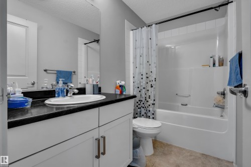 Bathroom featuring a white vanity with a dark countertop, an undermount sink with a chrome faucet, a large wall mirror, and a white tub/shower combination with white subway tile surround - 128 390 Windermere Road, Edmonton, AB - Indoor Photo Showing Bathroom