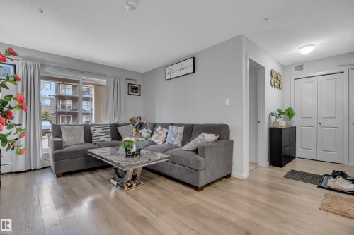 Open-concept living area featuring light wood-finish flooring, a sliding glass door to a private balcony, and light gray painted walls - 128 390 Windermere Road, Edmonton, AB - Indoor Photo Showing Living Room