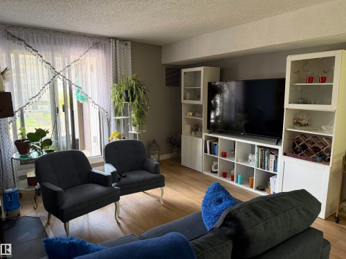 Living area featuring wood-finish flooring, a full-wall built-in media center, and expansive glass doors opening to the outdoors - 205 10604 110 Avenue Nw, Edmonton, AB - Indoor Photo Showing Living Room
