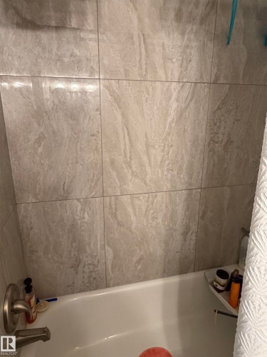 Bathtub with brushed nickel fixtures and light-toned tile surround - 205 10604 110 Avenue Nw, Edmonton, AB - Indoor Photo Showing Bathroom