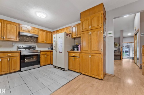 Kitchen featuring extensive wood cabinetry, tile flooring, stainless steel range with overhead hood, and a decorative tile backsplash - 4231 32 Avenue, Edmonton, AB - Indoor Photo Showing Kitchen