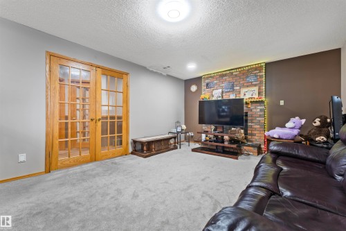 Living area featuring light grey carpeting, a brick-faced fireplace, a brown accent wall, and a textured ceiling - 4231 32 Avenue, Edmonton, AB - Indoor